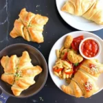 Savory crescent rolls served with pasta, nuggets, and dipping sauce on a black marble background.