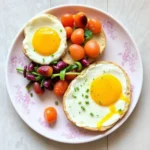 A plate with sunny-side-up eggs on toasted bread, served with cherry tomatoes and a side of kidney bean salad.